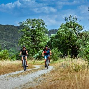 Fünf-Flüsse-Radweg: Radfahrer auf einem Kiesweg umgeben von grünen Hügeln und Bäumen